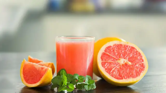 Szklanka soku grejpfrutowego, połówka grejpfruta i ćwiartki owocu z listkami mięty. Pamiętaj o interakcji soku grejpfrutowego a leki.