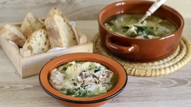 Two bowls of hearty Italian soup with greens and meat, served with crusty bread in a wooden crate.