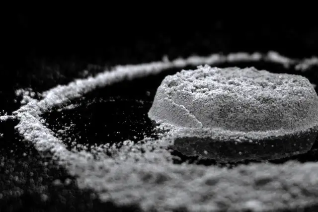 Biały proszek uformowany w kopczyk i linię na czarnym tle.