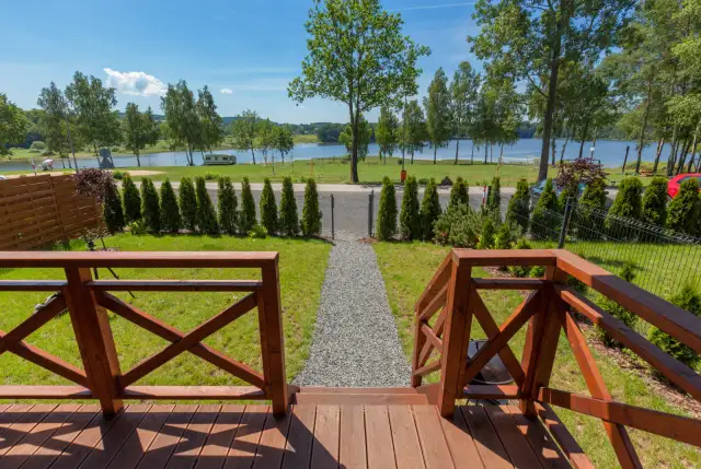 Drewniany taras z widokiem na jezioro, drzewa i zielony trawnik.