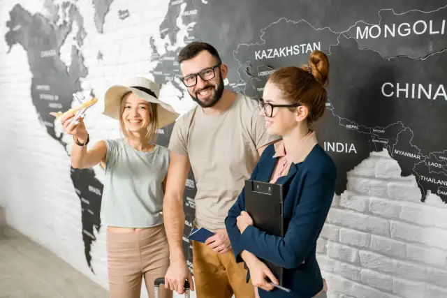 Para z paszportem i modelką samolotu przed mapą świata, obok pracownicy biura podróży.