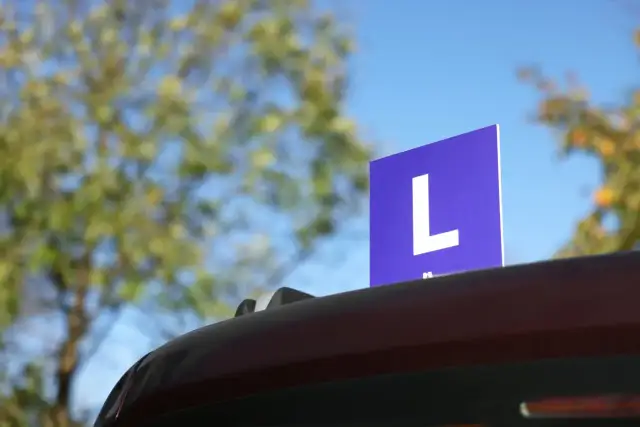 Niebieska tabliczka z literą "L" na dachu samochodu, symbolizująca naukę jazdy. Czy to zapowiedź najtrudniejszych pytań na prawo jazdy kat B?