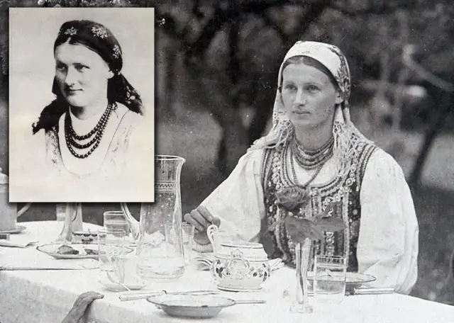 Chłopomania w weselu: młoda kobieta w tradycyjnym stroju, z naszyjnikami i chustą na głowie, siedzi przy stole nakrytym do obiadu.