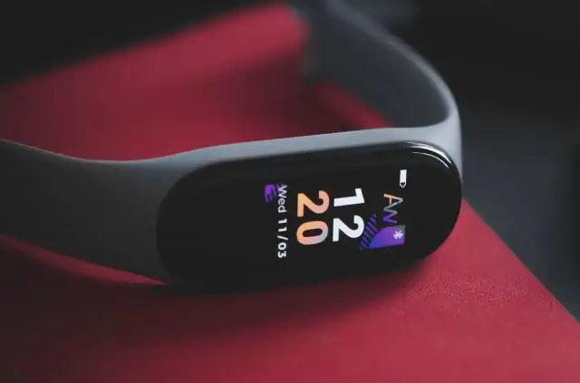 Szary smartband do pływania na czerwonym tle. Wyświetla godzinę 12:20 i datę.