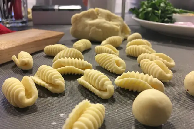 Świeży, domowy makaron w kształcie muszelek i innych form, leżący na szarej powierzchni.