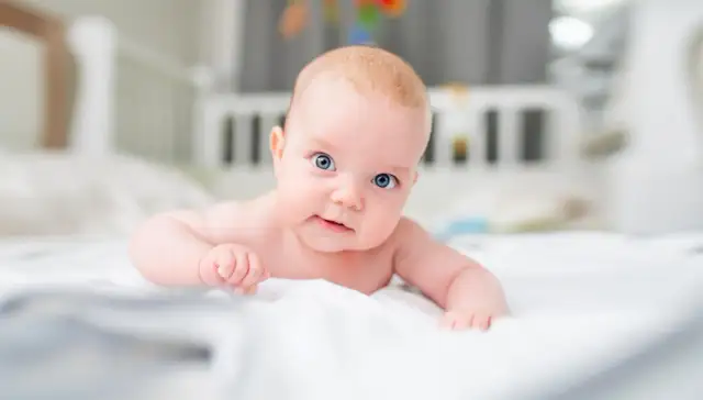 Niebieskooki, 3-miesięczny maluch leży na brzuchu, ćwicząc mięśnie szyi.