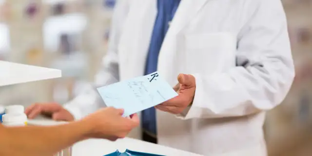 Farmaceuta w białym fartuchu podaje receptę. Dowiedz się, jak odzyskać kod recepty, aby zrealizować leki.