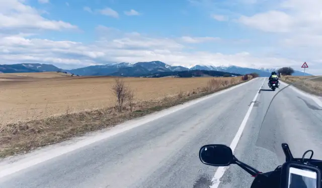 Motocykliści jadący drogą w kierunku ośnieżonych gór Tatr.