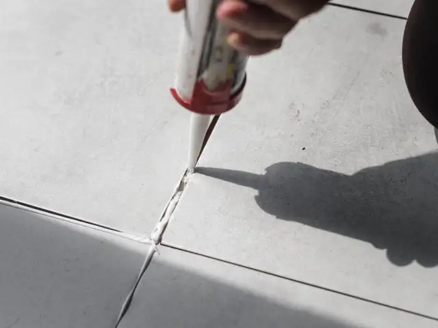 Ręka z pistoletem wyciska masę uszczelniającą w szczelinę między płytkami, rozpoczynając wymianę fugi.