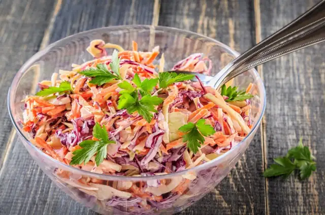 Surówka z białej i czerwonej kapusty z marchewką, udekorowana natką pietruszki, w szklanej misce.