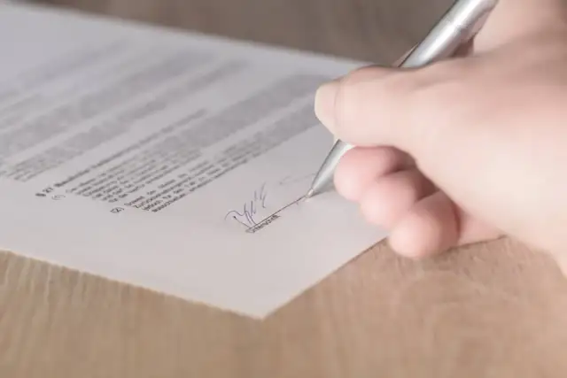 Dłoń podpisuje dokument srebrnym długopisem.