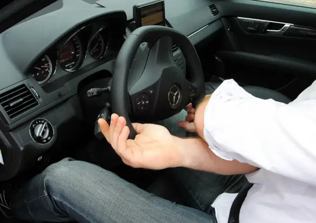 Dłoń kierowcy na kierownicy, słychać skrzypienie przy skręcaniu. Widoczny fragment deski rozdzielczej i siedzenia.