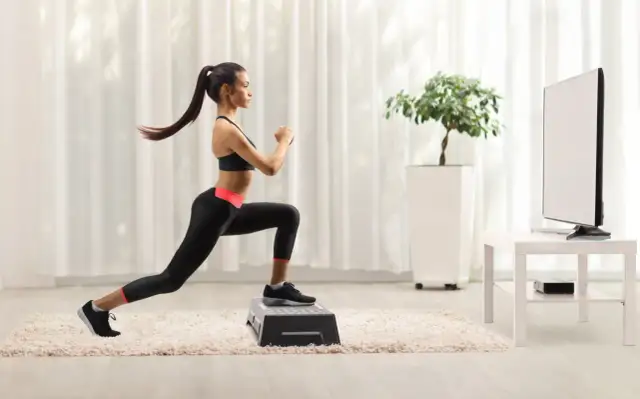 Kobieta wykonuje wykroki na stopniu, ćwicząc w domu. To świetny przykład, jak zacząć trening interwałowy co to jest i jak go stosować.