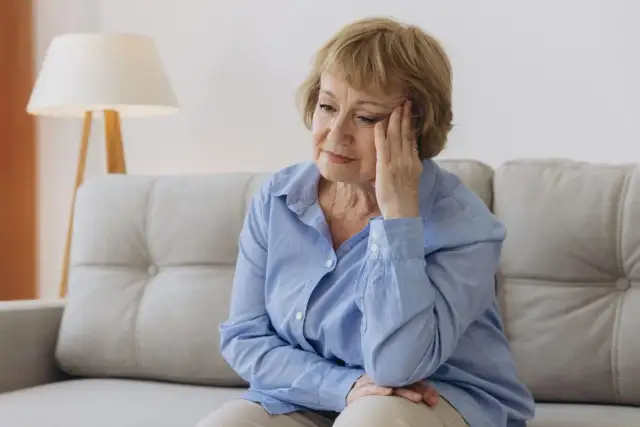 Zamyślona starsza pani siedzi na kanapie, zastanawiając się, co odpisać na tęsknię.