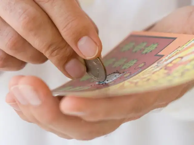 Dłoń zdrapuje monetą zdrapkę z symbolem dolara.