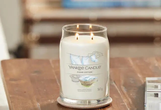 Zapalone świece zapachowe Yankee Candle Clean Cotton w szklanym słoju na drewnianym stole.