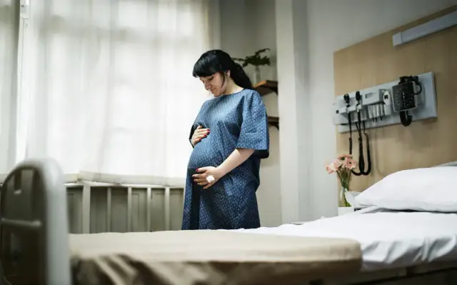 Kobieta w szpitalnej sali, trzymająca się za brzuch, szuka sposobów, jak złagodzić skurcze porodowe.