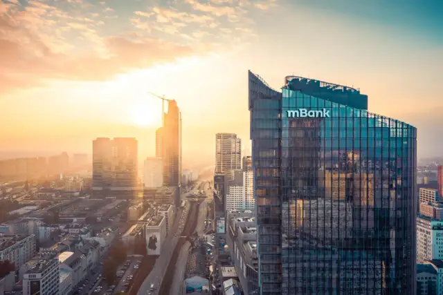 Zachód słońca nad miastem, z dominującym budynkiem mBank. Zastanawiasz się, ile trwa sesja przychodząca w mBanku?