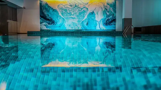 Relaks w nowoczesnym spa pod Poznaniem. Błękitna woda basenu odbija abstrakcyjną, turkusowo-żółtą mozaikę na ścianie.