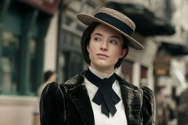 Młoda kobieta w kapeluszu i aksamitnej marynarce, jakby wyruszyła na polowanie na ćmy w wiktoriańskim mieście.