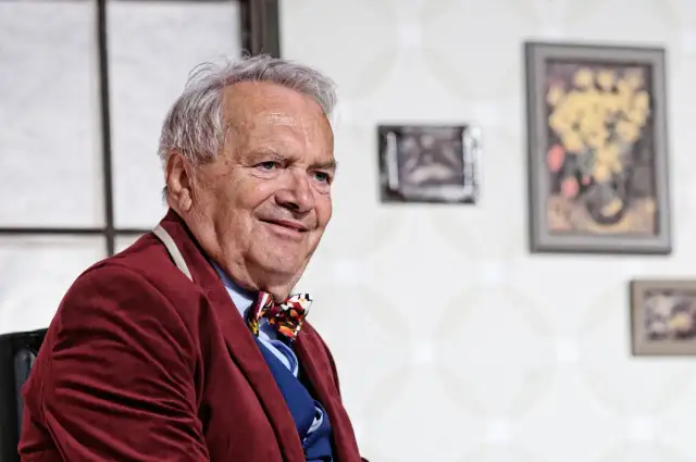 Uśmiechnięty Zdzisław Wardejn, znany z wielu filmów, w bordowym marynarkowym stroju i kolorowym krawacie.