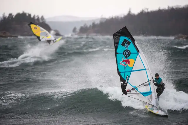 Windsurferzy na falach, jeden z nich na pierwszym planie, w akcji.
