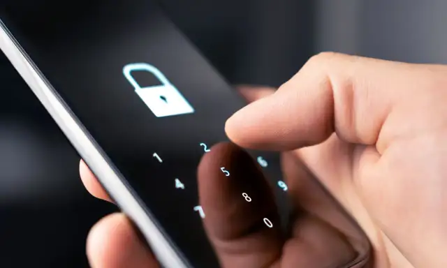 Dłoń wpisuje kod na ekranie telefonu, symbolizując jak zmienić kod w domofonie w bloku.