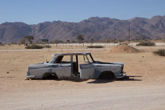 Zardzewiały wrak samochodu na pustyni, jak po aukcjach PZU samochody powypadkowe. Góry w tle.