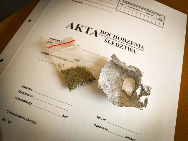 Mała torebka z suszem i grudka substancji w folii aluminiowej na dokumentach śledczych.