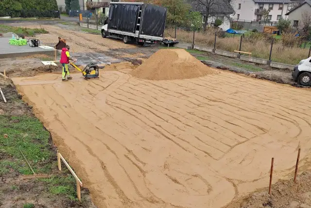 Pracownik zagęszcza piasek zagęszczarką. To kluczowy etap wymiany gruntu pod płytę fundamentową.