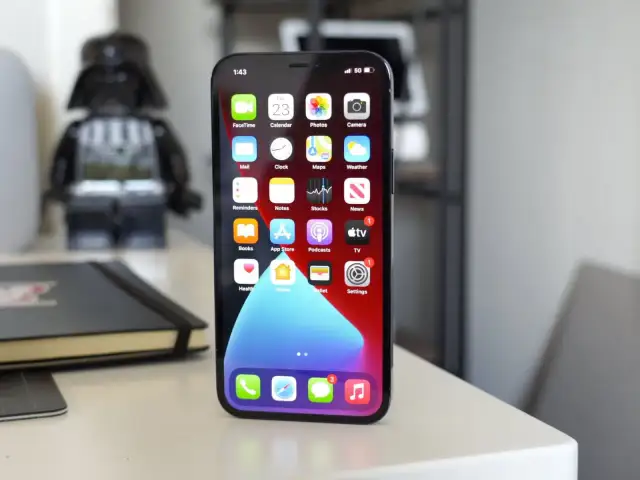 iPhone 11 z widocznym wskaźnikiem 5G na ekranie, na biurku obok figurki Dartha Vadera.