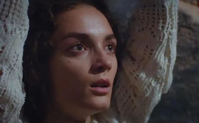 Twarz młodej kobiety, pełna emocji, w białym, dzianinowym szalu. Scena z serialu "Dziedzictwo", turecki serial.