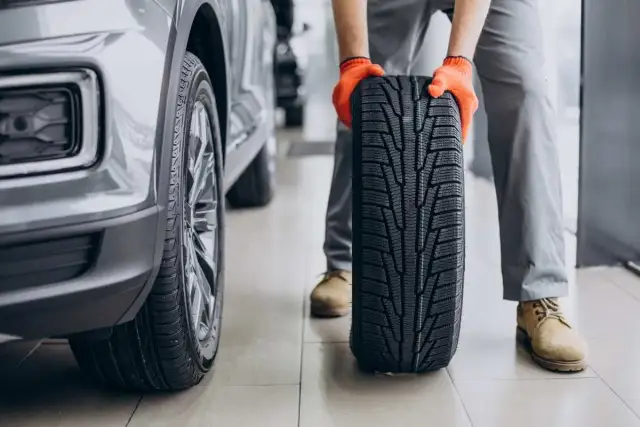 Mechanik w pomarańczowych rękawiczkach trzyma nowe opony letnie obok samochodu. Czas na test opon letnich!