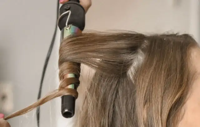 Dłoń nawija brązowe włosy na lokówkę, tworząc falę.