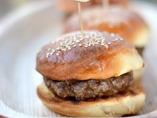 Mini burger z sezamową bułką i kotletem na talerzu.