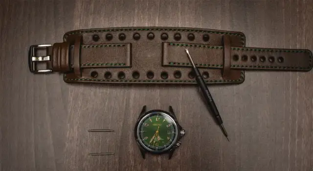 Zegarek z zieloną tarczą, brązowy pasek, narzędzie i teleskopy na drewnianym tle.