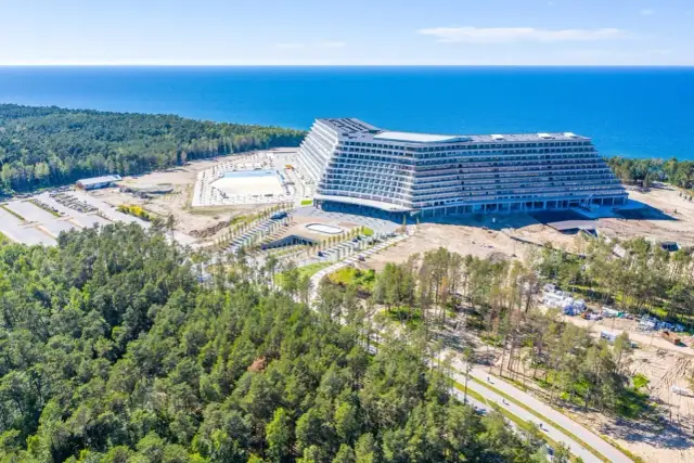 Nowoczesny hotel z basenem i widokiem na morze, otoczony lasem.