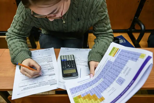 Uczeń pisze egzamin, przed nim leżą arkusze z zadaniami, kalkulator i układ okresowy pierwiastków.