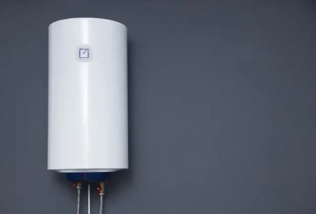 Biały bojler elektryczny wiszący na szarej ścianie.