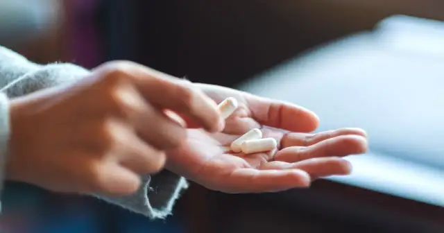 Dłoń trzyma kilka białych kapsułek. Czy to początek problemów z przedawkowanie witaminy B12 objawy?