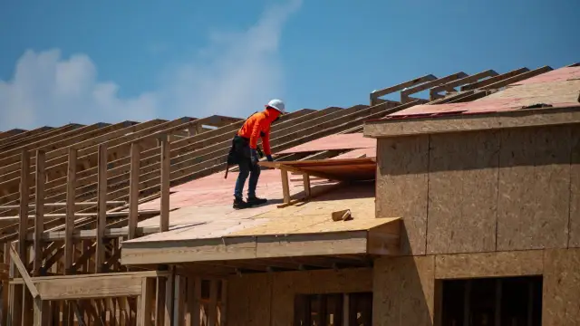 Dekarz w pomarańczowej bluzie i białym kasku pracuje na budowie dachu.