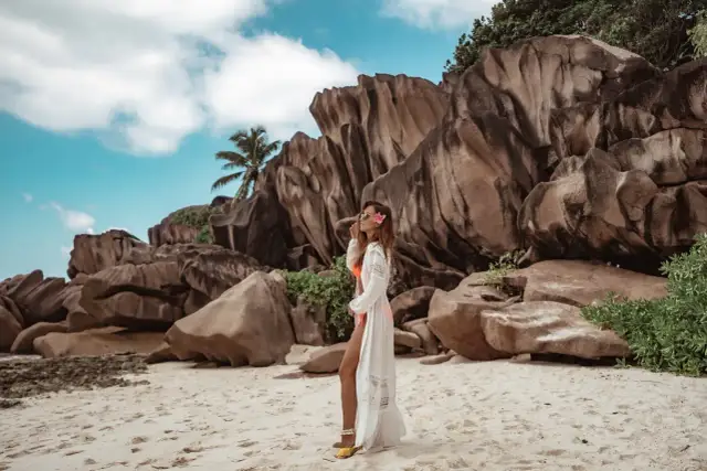 Kobieta w białej narzutce na plaży z granitowymi skałami w tle. Seszele atrakcje to raj dla miłośników przyrody i pięknych krajobrazów.
