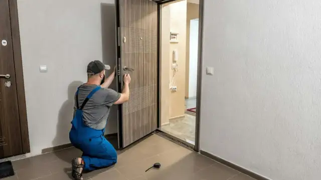 Monter w niebieskich ogrodniczkach montuje drzwi zewnętrzne, klamiąc klamkę.