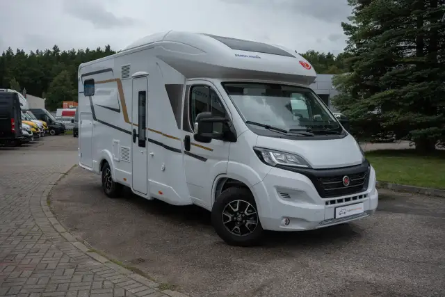 Biały van camper z brązowymi i czarnymi akcentami, zaparkowany na zewnątrz. Idealny do podróży i odkrywania nowych miejsc.