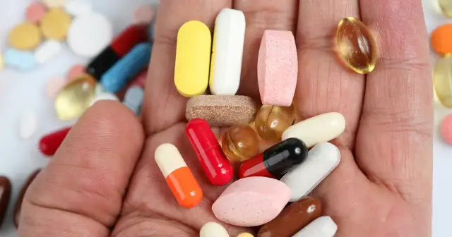 Dłoń pełna tabletek i kapsułek, w tym pomarańczowo-biała, żółta, różowa i czerwona. Może to być pomoc w walce z bólem co na stawy.