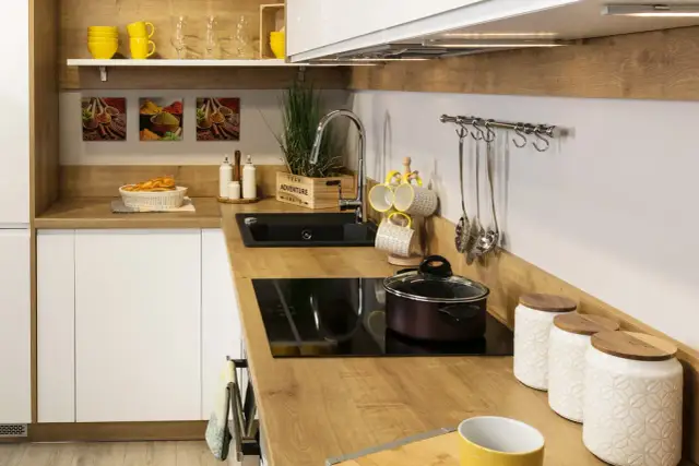 Nowoczesna kuchnia z drewnianym blatem, czarnym zlewem i płytą indukcyjną.