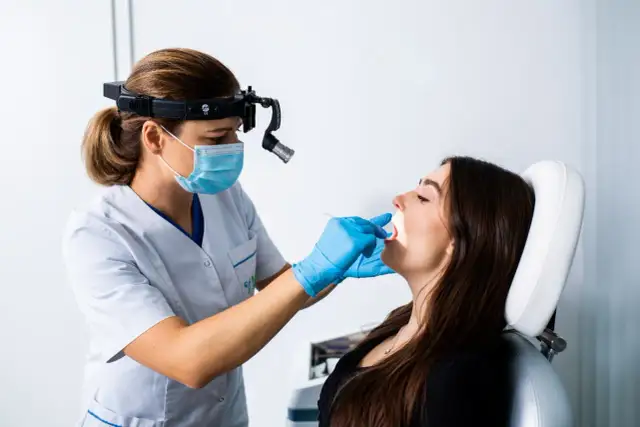 Lekarz bada gardło pacjentki. Ile dni L4 na anginę ropną w Polsce?