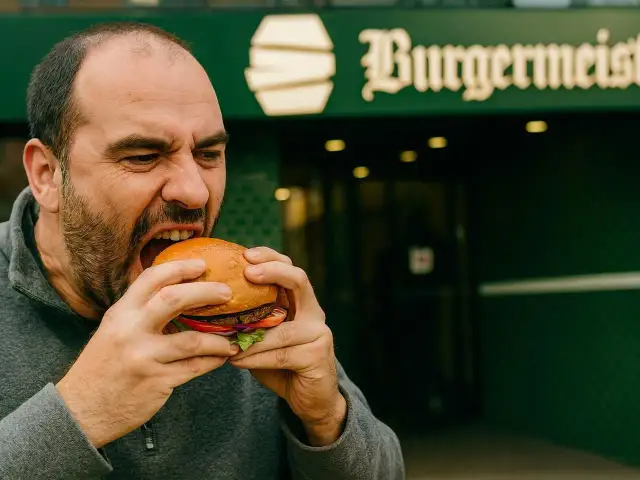 Mężczyzna z pasją wgryza się w soczystego burgera, zastanawiając się, skąd pochodzą hamburgery.