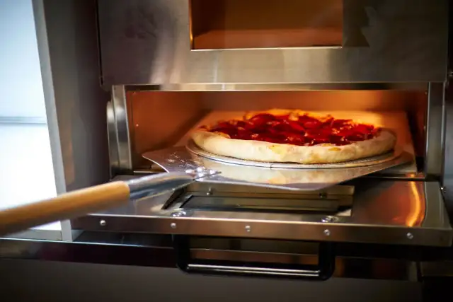 Pizza z pepperoni na łopacie wkładana do pieca.