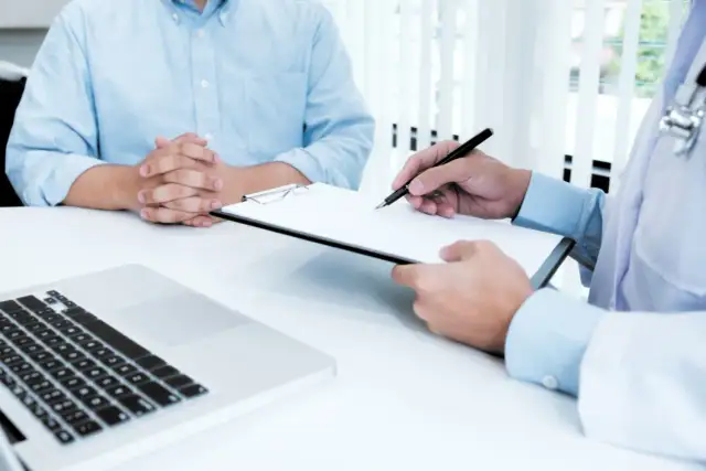 Lekarz pisze na kartce, pacjent siedzi naprzeciwko.